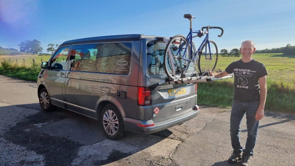 Member of Four Seasons Campers crew with his bike on the back of a campervan showing we offer bike rack hire