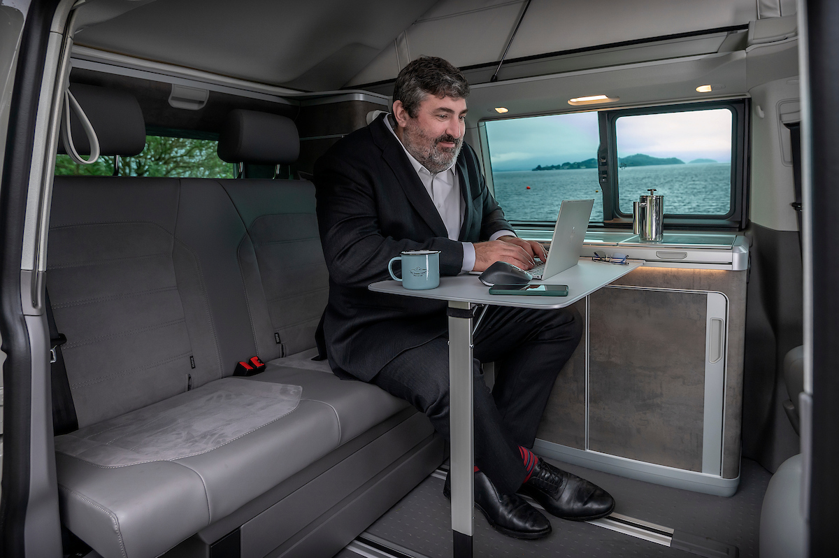 Interior campervan with man using as office with laptop and coffee and loch view with Four Seasons Campers corporate travel acccomodation