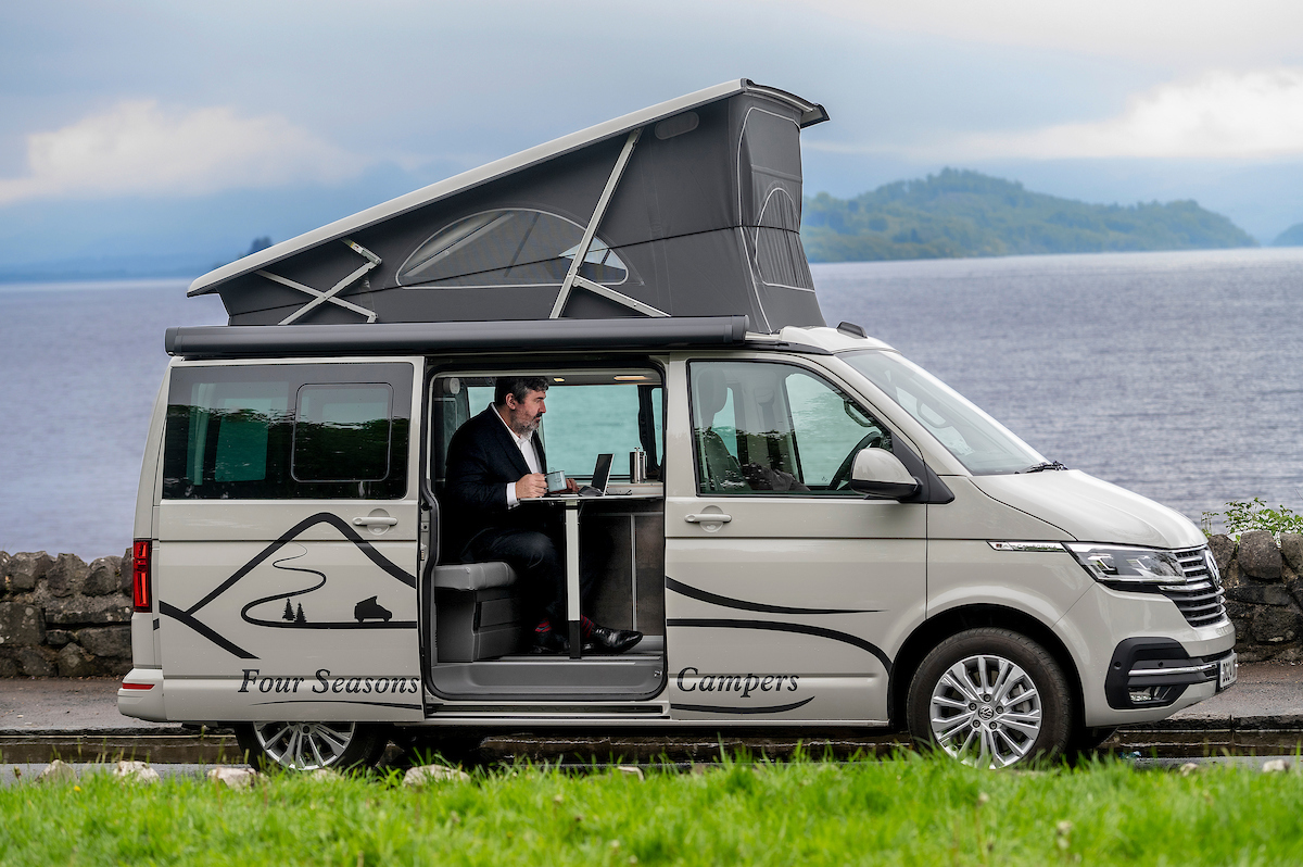 corporate travel employee in suit in campervan with pop up roof by loch in Scotland for business travel accommodation with Four Seasons Campers