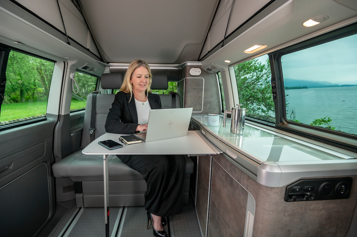 woman in suit typing laptop in campervan with pop up roof by loch in Scotland for business travel accommodation with Four Seasons Campers