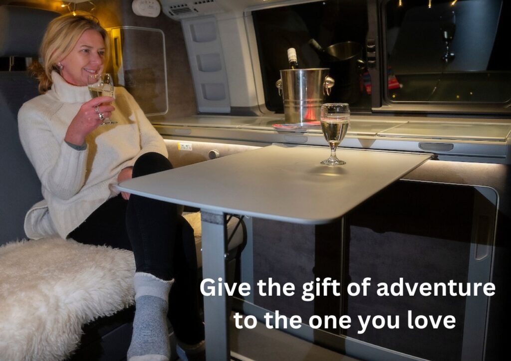 woman in campervan with glass of wine and table up for a campervan treat with gift voucher present