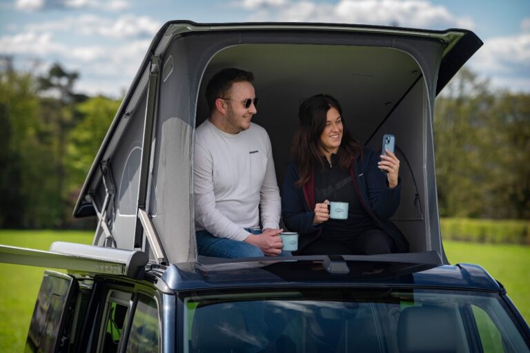 man and woman in roof of campervan pop up roof at Four Seasons Campers with girl holding phone