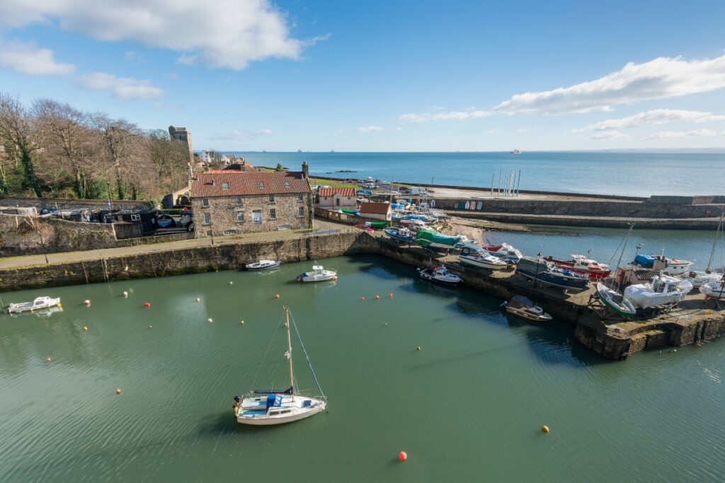 Dysart Harbour Scotland with sailing boat in sea and boats and harbour wall with old house with red roof