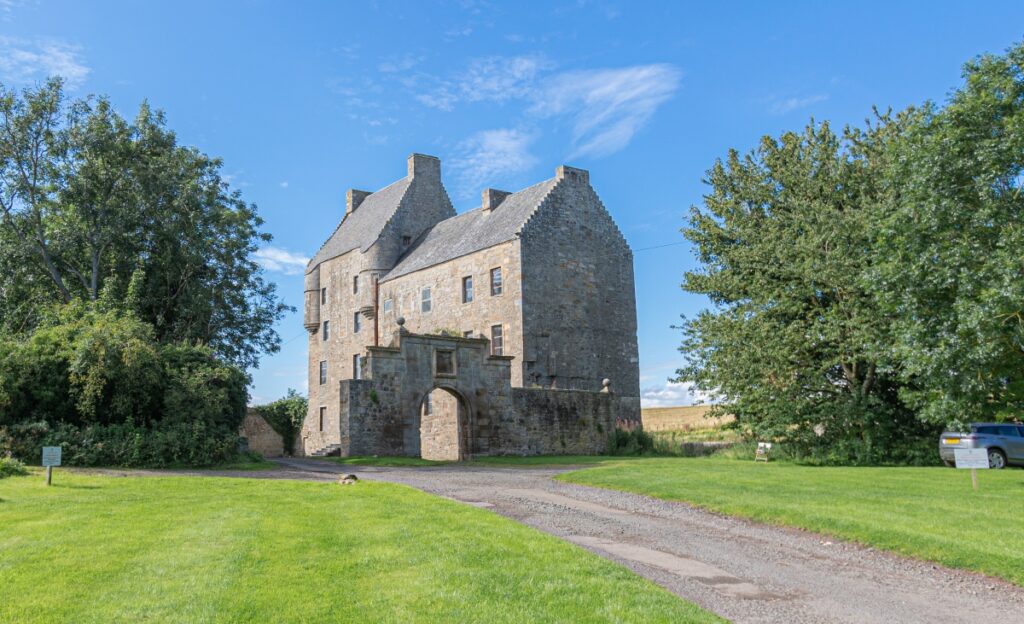 Midhope Castle by Hopetoun House in Edinburgh with driveway to arch entrance to walled garden and tower surrounded by green trees