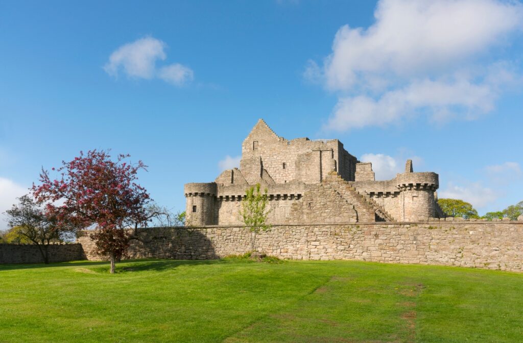 Craigmillar Caslte with wall around castle and grass and red tree in Scotland