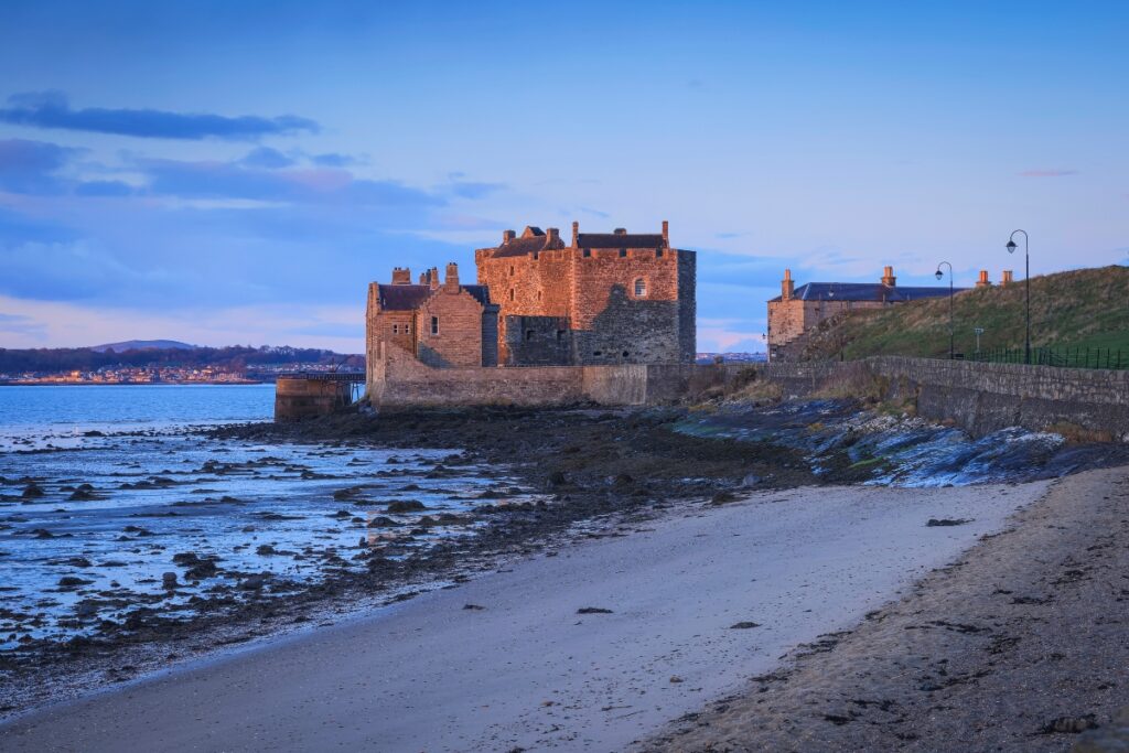 Blackness Castle beside sea and beach in the dusk with castle lit up near Edinburgh