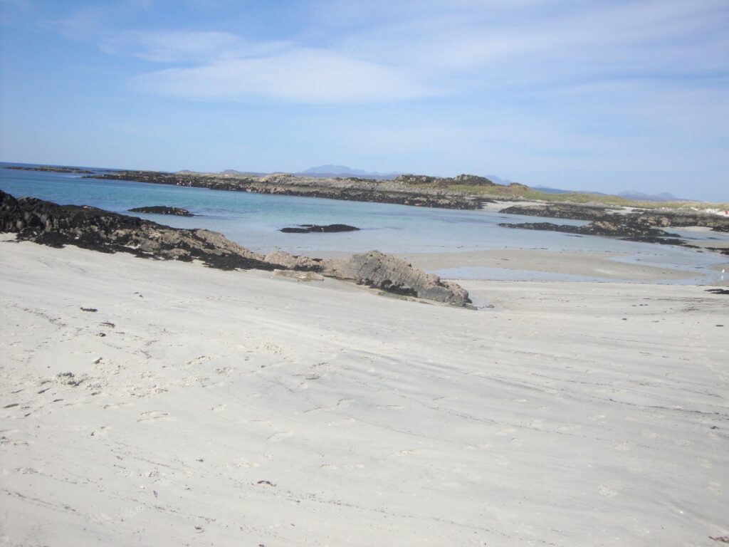 Beach at Arisaig with white sand and rocks and blue sky near Skye Scotland