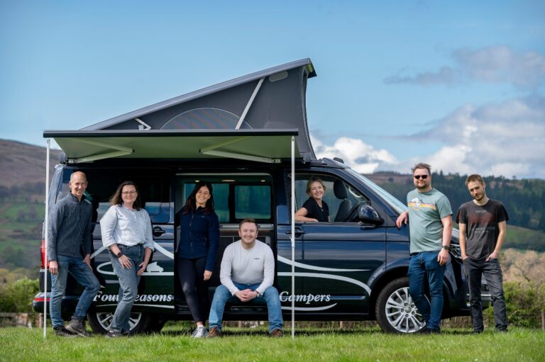 6 members of staff of Four Seasons Campers campervan hire scotland in campervan with awning and pop up roof in field