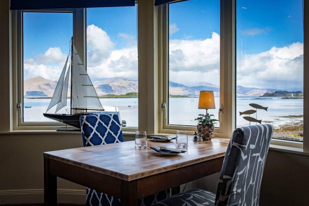 table and chairs in pierhouse hotel with view out to loch linhee and sailing boat in window