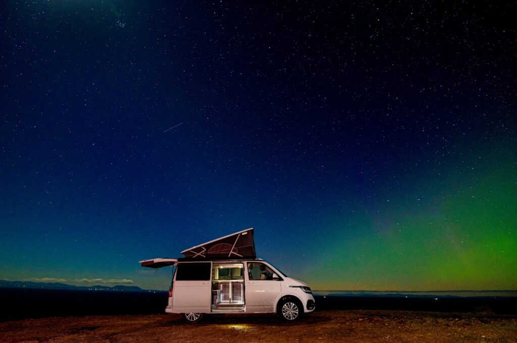 starry night sky with green glow of aurora with white Four Seasons Campers campervan at Gairloch Scotland