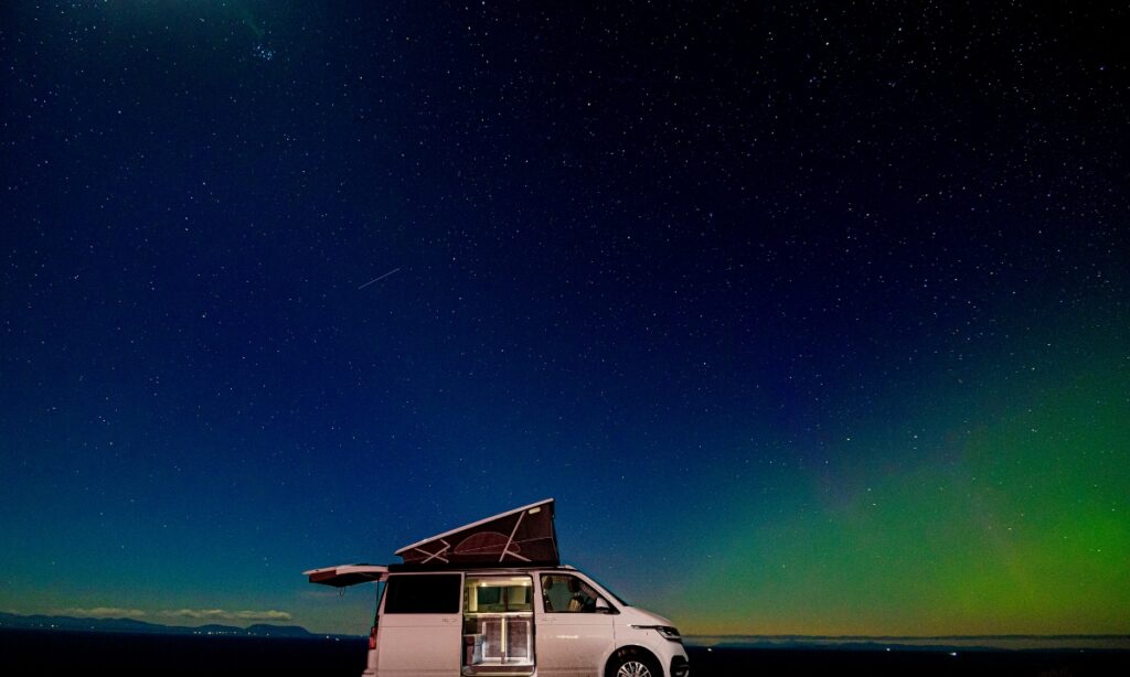 starry night sky with green glow of aurora with white Four Seasons Campers campervan at Gairloch Scotland