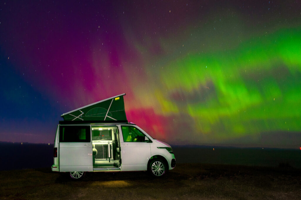 white campervan with aurora northern lights of red and green at Gairloch Scotland