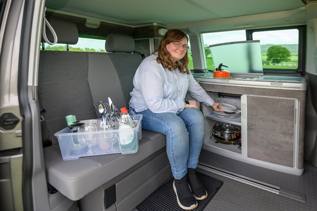 Manager Four Seasons Campers in campervan putting kitchen equipment in cupboard