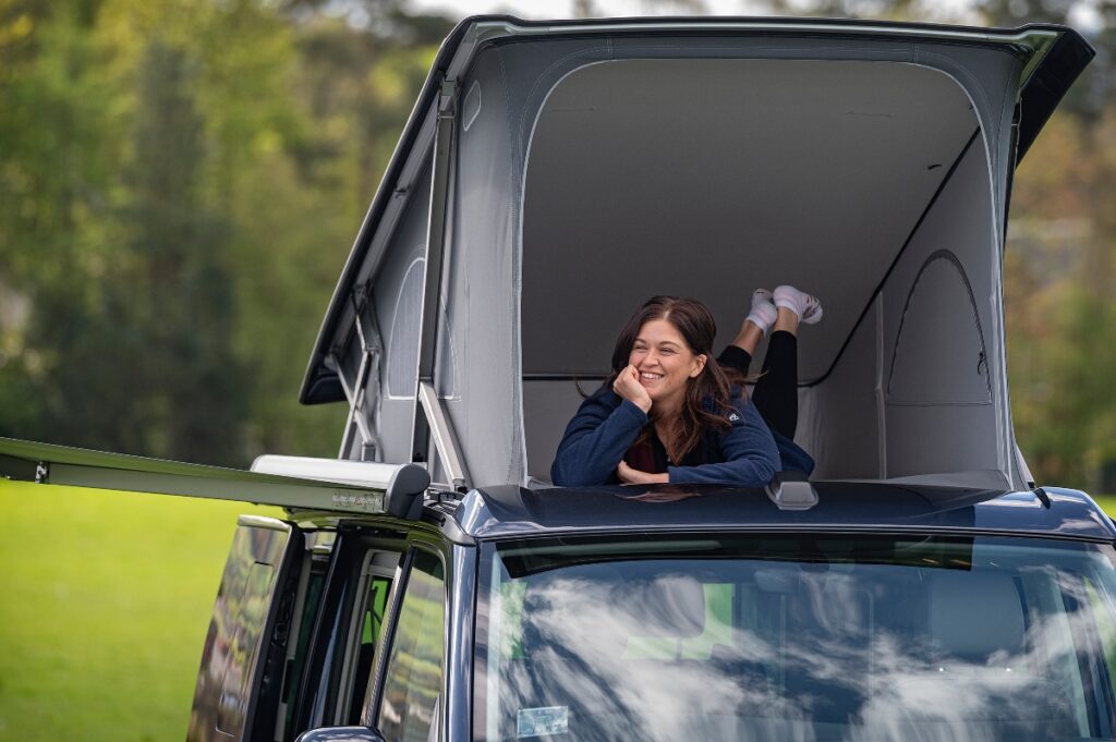 best campervan for star gazing - girl in pop up roof of campervan lying down with legs in air and opened front of roof